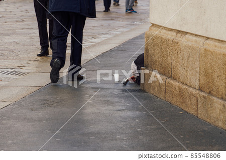 Unidentified beggar with hidden facial details on the streets of Milan, Italy.  85548806