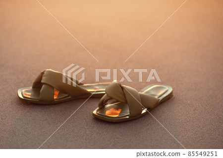 Female leather flat sandals on the beach. Sunset summer background Female leather flat sandals on the beach. Sunset summer background 85549251