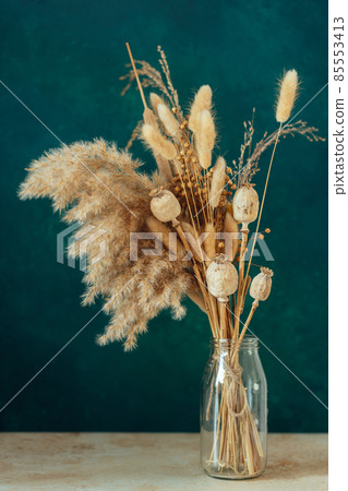 Bouquet of beige dried flowers in a glass vase on green-blue background. Bouquet of beige dried flowers in a glass vase on green-blue background. 85553413