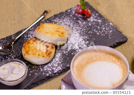 Cheesecakes with strawberries. Two fried curds on a black tray. Close-up. 85554121