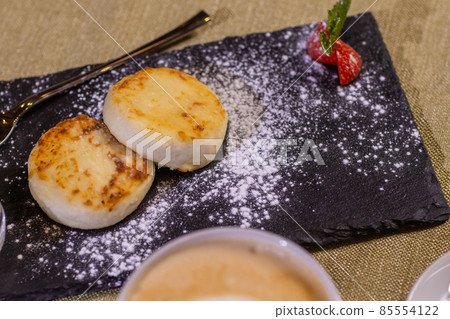 Cheesecakes with strawberries. Two fried curds on a black tray. Close-up. 85554122