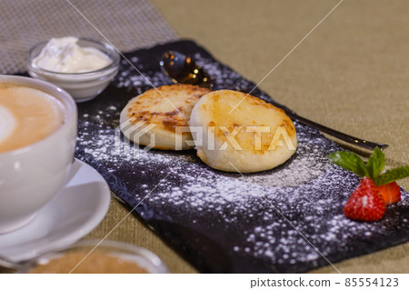Cheesecakes with strawberries. Two fried curds on a black tray. Close-up. 85554123