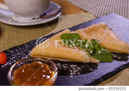 Pancakes, flat and round flour products made from batter by frying in a pan, lie on a black slate plate against a gray background. Pancakes are used as an independent dish and together with fillings. Pancakes, flat and round flour products made from batter by frying in a pan, lie on a black slate plate against a gray background. Pancakes are used as an independent dish and together with fillings. 85554131
