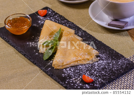 Pancakes, flat and round flour products made from batter by frying in a pan, lie on a black slate plate against a gray background. Pancakes are used as an independent dish and together with fillings. Pancakes, flat and round flour products made from batter by frying in a pan, lie on a black slate plate against a gray background. Pancakes are used as an independent dish and together with fillings. 85554132