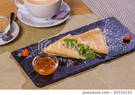 Pancakes, flat and round flour products made from batter by frying in a pan, lie on a black slate plate against a gray background. Pancakes are used as an independent dish and together with fillings. Pancakes, flat and round flour products made from batter by frying in a pan, lie on a black slate plate against a gray background. Pancakes are used as an independent dish and together with fillings. 85554133