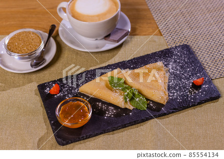 Pancakes, flat and round flour products made from batter by frying in a pan, lie on a black slate plate against a gray background. Pancakes are used as an independent dish and together with fillings. Pancakes, flat and round flour products made from batter by frying in a pan, lie on a black slate plate against a gray background. Pancakes are used as an independent dish and together with fillings. 85554134