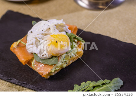 Poached egg on toast, with smoked salmon, avocado, grilled tomato, and baby spinach. 85554136