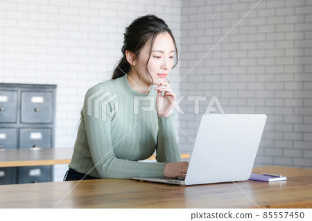 A Japanese woman who thinks with a serious look while looking at a computer. There is a copy space. 85557450