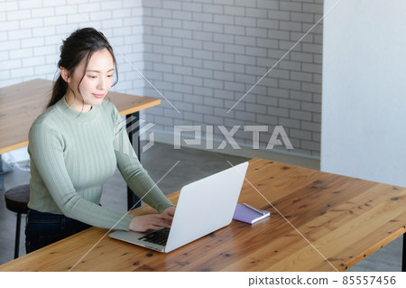 A Japanese woman typing with a smile while looking at a computer. There is a copy space. A little bird's-eye view. A Japanese woman typing with a smile while looking at a computer. There is a copy space. A little bird's-eye view. 85557456