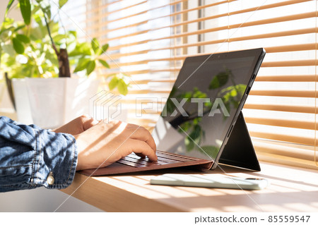 陽光明媚的日子，一個男人在窗邊用電腦工作 85559547