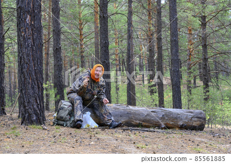 A woman, picking mushrooms, sat down to rest on a fallen tree in a pine forest A woman, picking mushrooms, sat down to rest on a fallen tree in a pine forest 85561885