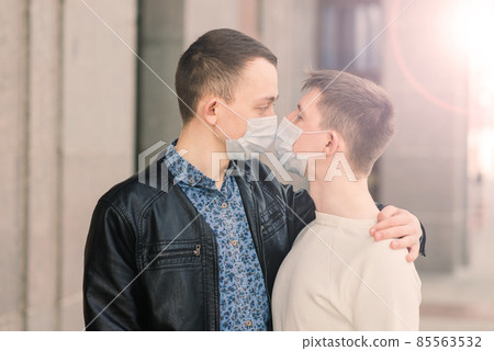 Young gay couple wearing medical mask hugging at city. Young gay couple wearing medical mask hugging at city. 85563532