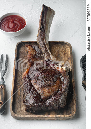 Steak on the bone. tomahawk steak freshly grilled dry aged BBQ food, on wooden serving board, on white stone background Steak on the bone. tomahawk steak freshly grilled dry aged BBQ food, on wooden serving board, on white stone background 85564889