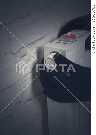 A woman's hand in winter gloves holds the handle of the heating thermostat. The concept of the cost of heating services, the increase in prices for utilities. Lack of heat. A woman's hand in winter gloves holds the handle of the heating thermostat. The concept of the cost of heating services, the increase in prices for utilities. Lack of heat. 85566793