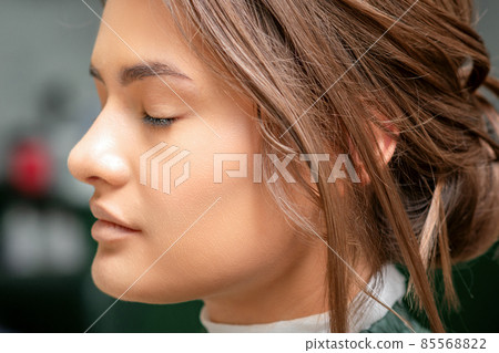 Portrait of a sensual young caucasian woman with closed eyes showing makeup tan on her face and hairstyle in a beauty salon. 85568822