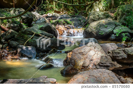 Clean and pure water streams in the creek flow through the rock boulders, Beraliya tropical rainforest. Peaceful natural scenery landscape shot. Clean and pure water streams in the creek flow through the rock boulders, Beraliya tropical rainforest. Peaceful natural scenery landscape shot. 85570080