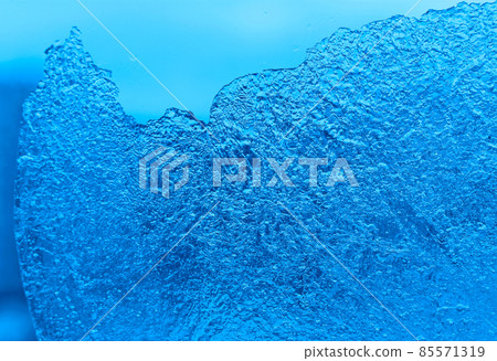 Piece of ice on glass background. Close-up natural blue texture. 85571319