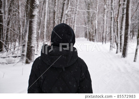 A woman walks alone in a snow-covered park among trees. A woman walks alone in a snow-covered park among trees. 85572983