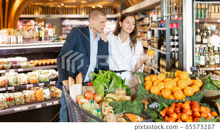 Happy young couple with a grocery cart in the supermarket shooses tangerines 85573287