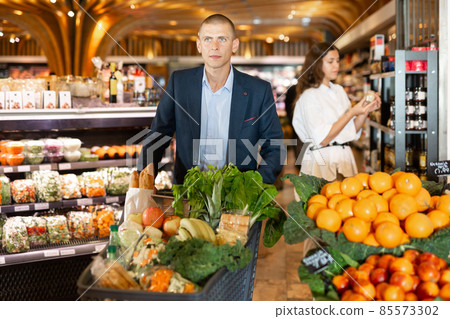 Portrait of a focused young male with a grocery cart in the supermarket 85573302
