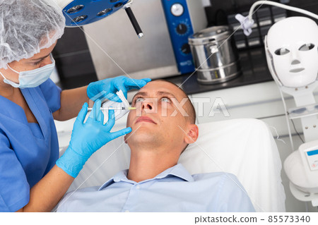 Man receiving cosmetic facial injection in clinic Man receiving cosmetic facial injection in clinic 85573340