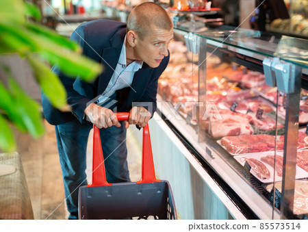 Focused man examines the production in the department of the butcher shop in the supermarket 85573514