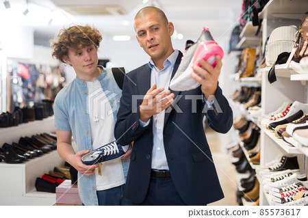 Teenager looking for sneakers with help of sales assistant Teenager looking for sneakers with help of sales assistant 85573617