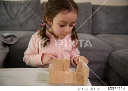 Adorable Caucasian 4 years old baby girl building house with wooden bricks and blocks. Hand movement control and concentration skills concept, educational board games Adorable Caucasian 4 years old baby girl building house with wooden bricks and blocks. Hand movement control and concentration skills concept, educational board games 85574534