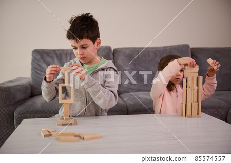 Creative children, brother and sister concentrated on building from wooden blocks, playing developmental board games, building complex tall wooden structures at home. Educational leisure and pastime Creative children, brother and sister concentrated on building from wooden blocks, playing developmental board games, building complex tall wooden structures at home. Educational leisure and pastime 85574557