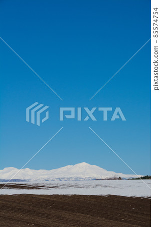 Fields with residual snow, snowy mountains and blue sky Daisetsuzan 85574754