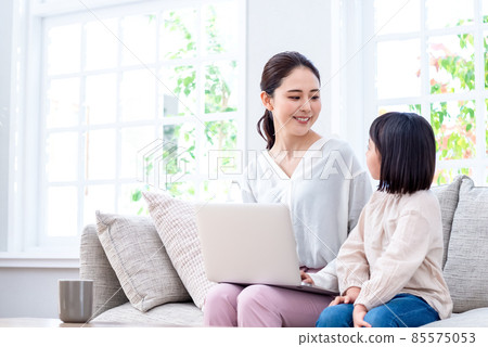 A child sitting on the couch and talking to his mother operating a laptop A child sitting on the couch and talking to his mother operating a laptop 85575053