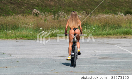 Caucasian woman in bikini rides a bike on a hot summer day. Caucasian woman in bikini rides a bike on a hot summer day. 85575160