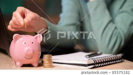 The girl puts her savings in a piggy bank. 85575182