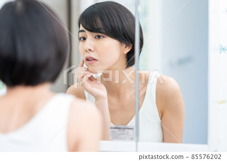 一個女人在鏡子裡檢查她的皮膚狀況 85576202