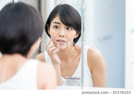 A woman checking the condition of her skin in the mirror A woman checking the condition of her skin in the mirror 85576203
