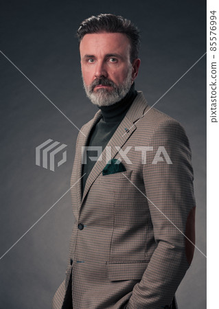 Portrait of a stylish elegant senior businessman with a beard and casual business clothes in photo studio isolated on dark background gesturing with hands Portrait of a stylish elegant senior businessman with a beard and casual business clothes in photo studio isolated on dark background gesturing with hands 85576994
