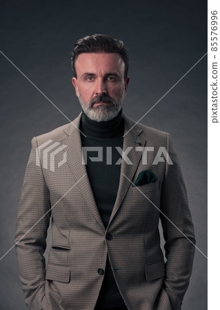 Portrait of a stylish elegant senior businessman with a beard and casual business clothes in photo studio isolated on dark background gesturing with hands Portrait of a stylish elegant senior businessman with a beard and casual business clothes in photo studio isolated on dark background gesturing with hands 85576996