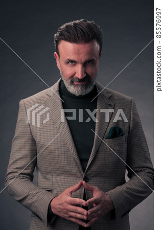 Portrait of a stylish elegant senior businessman with a beard and casual business clothes in photo studio isolated on dark background gesturing with hands Portrait of a stylish elegant senior businessman with a beard and casual business clothes in photo studio isolated on dark background gesturing with hands 85576997