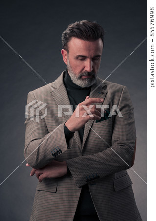 Portrait of a stylish elegant senior businessman with a beard and casual business clothes in photo studio isolated on dark background gesturing with hands Portrait of a stylish elegant senior businessman with a beard and casual business clothes in photo studio isolated on dark background gesturing with hands 85576998