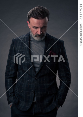 Portrait of a stylish elegant senior businessman with a beard and casual business clothes in photo studio isolated on dark background gesturing with hands Portrait of a stylish elegant senior businessman with a beard and casual business clothes in photo studio isolated on dark background gesturing with hands 85577044