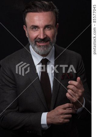 Portrait of a stylish elegant senior businessman with a beard and casual business clothes in photo studio adjusting suit Portrait of a stylish elegant senior businessman with a beard and casual business clothes in photo studio adjusting suit 85577045