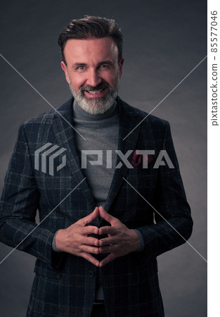 Portrait of a stylish elegant senior businessman with a beard and casual business clothes in photo studio isolated on dark background gesturing with hands Portrait of a stylish elegant senior businessman with a beard and casual business clothes in photo studio isolated on dark background gesturing with hands 85577046