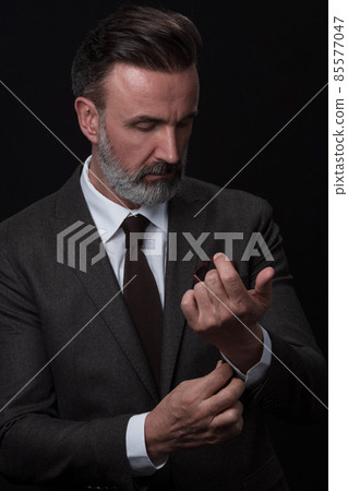 Portrait of a stylish elegant senior businessman with a beard and casual business clothes in photo studio adjusting suit 85577047