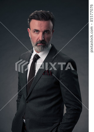 Portrait of a stylish elegant senior businessman with a beard and casual business clothes in photo studio isolated on dark background gesturing with hands Portrait of a stylish elegant senior businessman with a beard and casual business clothes in photo studio isolated on dark background gesturing with hands 85577076