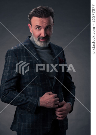 Portrait of a stylish elegant senior businessman with a beard and casual business clothes in photo studio isolated on dark background gesturing with hands Portrait of a stylish elegant senior businessman with a beard and casual business clothes in photo studio isolated on dark background gesturing with hands 85577077