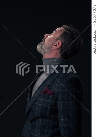 Portrait of a stylish elegant senior businessman with a beard and casual business clothes in photo studio isolated on dark background gesturing with hands Portrait of a stylish elegant senior businessman with a beard and casual business clothes in photo studio isolated on dark background gesturing with hands 85577078