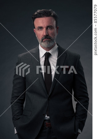 Portrait of a stylish elegant senior businessman with a beard and casual business clothes in photo studio isolated on dark background gesturing with hands Portrait of a stylish elegant senior businessman with a beard and casual business clothes in photo studio isolated on dark background gesturing with hands 85577079