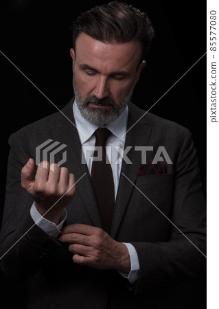 Portrait of a stylish elegant senior businessman with a beard and casual business clothes in photo studio adjusting suit Portrait of a stylish elegant senior businessman with a beard and casual business clothes in photo studio adjusting suit 85577080
