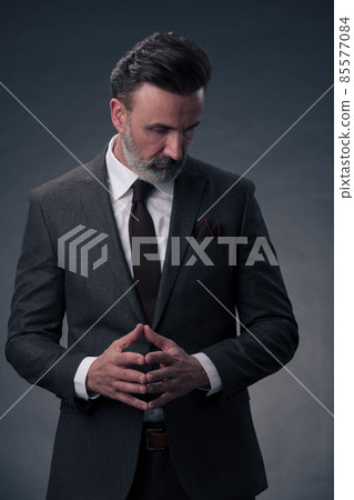 Portrait of a stylish elegant senior businessman with a beard and casual business clothes in photo studio isolated on dark background gesturing with hands Portrait of a stylish elegant senior businessman with a beard and casual business clothes in photo studio isolated on dark background gesturing with hands 85577084