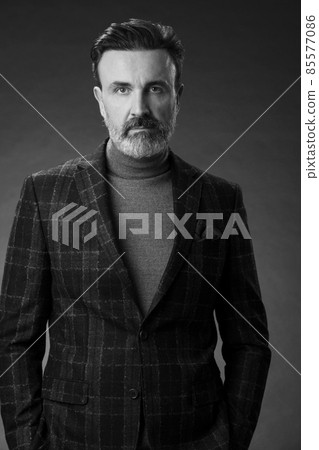 Portrait of a stylish elegant senior businessman with a beard and casual business clothes in photo studio isolated on dark background gesturing with hands 85577086